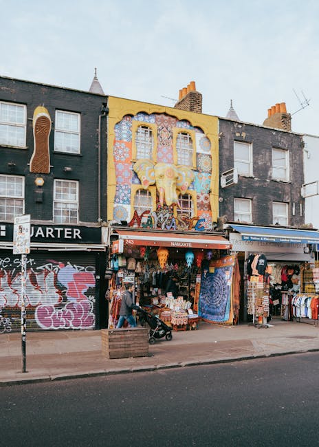 The image depicts a busy urban street scene in Camden Town, London, with a large railway bridge overhead bearing the prominent 'Camden Lock' sign painted in orange and yellow letters on a teal backgro